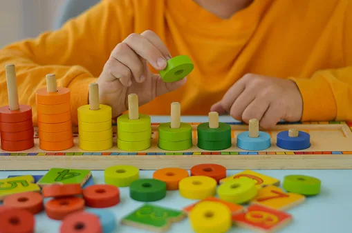 Math game for children. Children's hand plays with multi-colored rings. Natural materials, wooden. Score, number composition. Home education concept, early development, skills. Daylight.